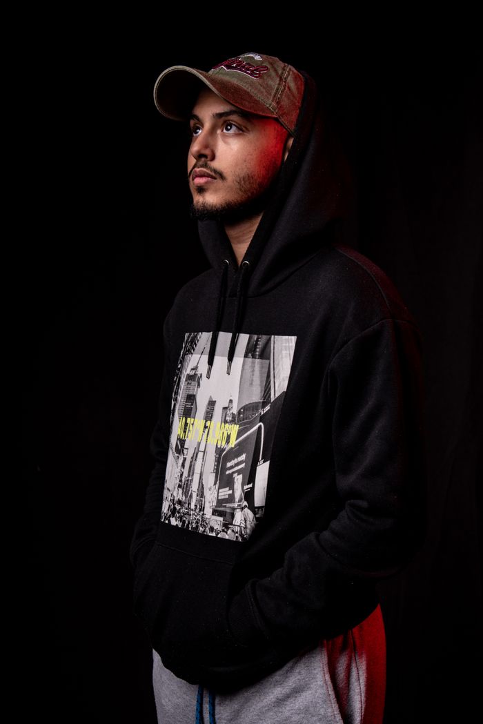 Studio portrait of a man wearing a black hoodie and cap against a dark background.