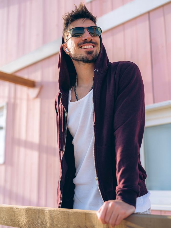 A stylish man in a hoodie and sunglasses leaning on a railing outdoors in Lisbon.