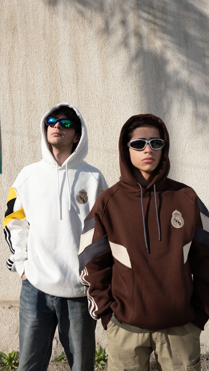 Two young adults wearing trendy hoodies and sunglasses standing outdoors.