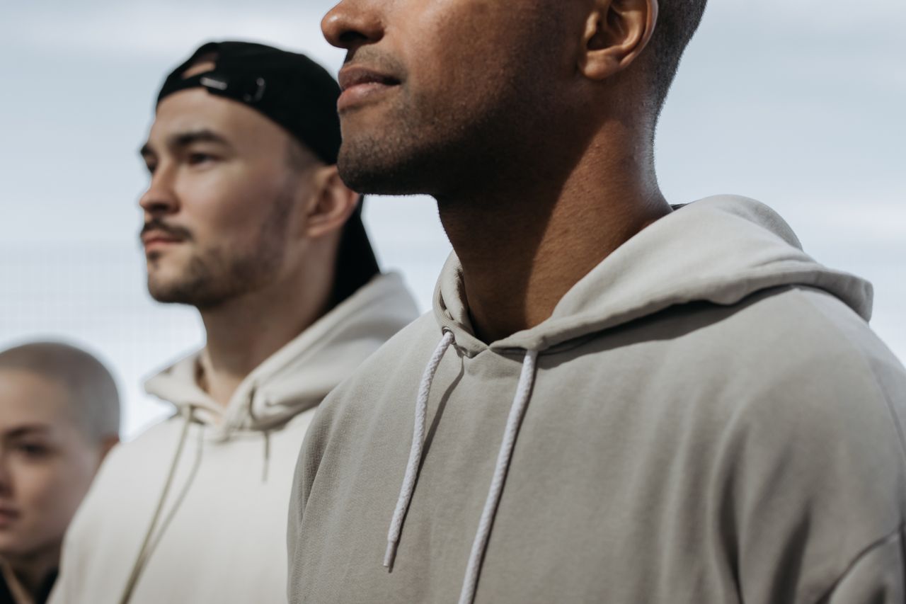 A diverse group of adults in hoodies stand outdoors exhibiting solidarity.