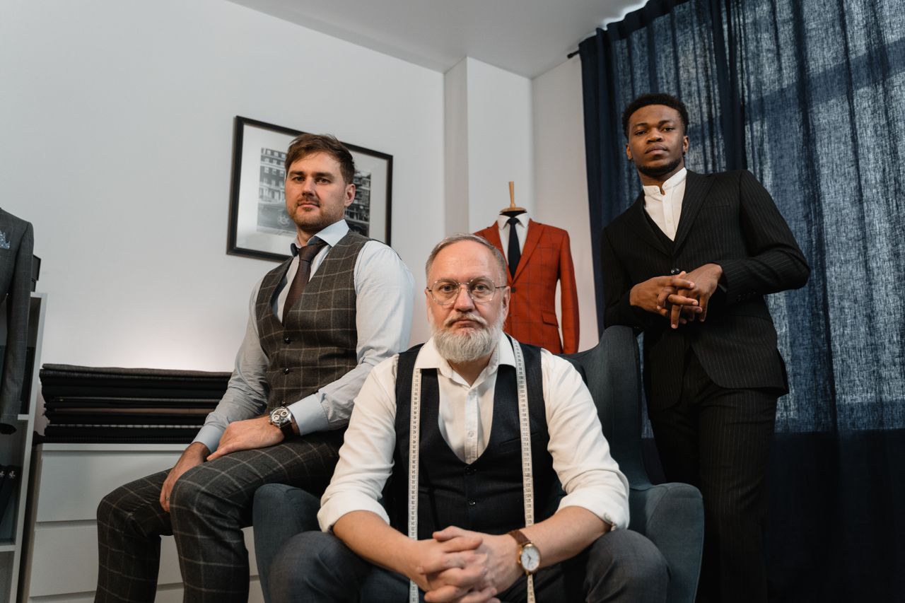 Three well-dressed men in an upscale tailor shop showcasing bespoke suits and elegance.