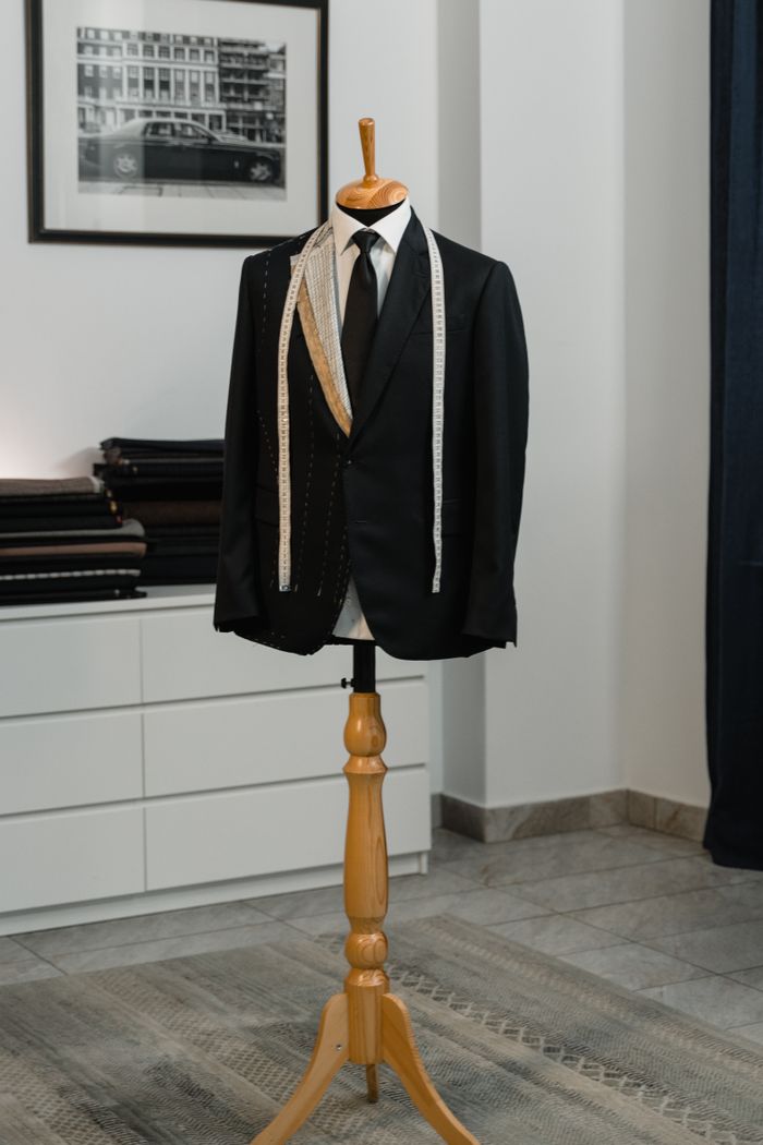 our-story-02 A stylish black suit jacket displayed on a mannequin with a measuring tape, showcasing bespoke tailoring in an elegant studio setting.
