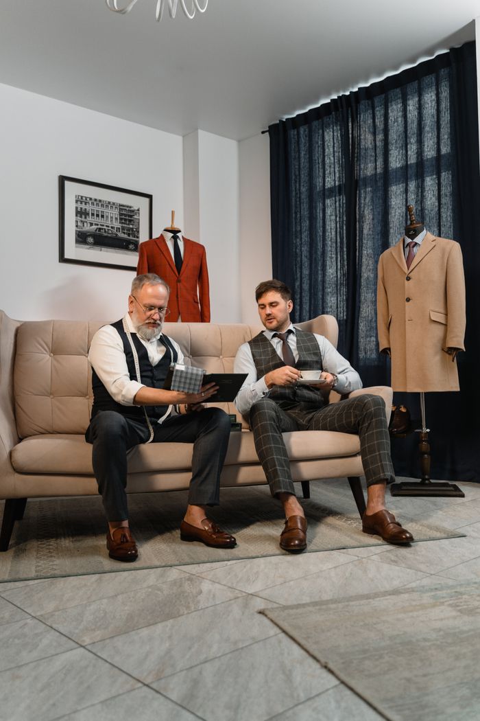 faq-img Professional tailor and client discussing bespoke suit designs in elegant workshop.